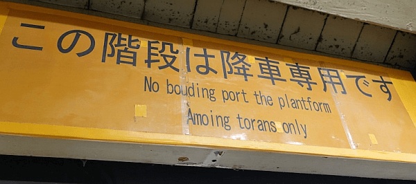 東京の渋谷駅構内の看板（2018年1月撮影）。上段には「この階段は降車専用です」とあり、下段1行目には“<em>No bouding port the plantform</em>”、2行目に“<em>Amoing torans only</em>” と記されている。